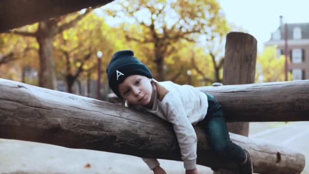 Милый мальчик веселится в парке приключений. Запутанный нервный ребенок в шляпе колеблется, застрял на канатах курс препятствие . — стоковое видео