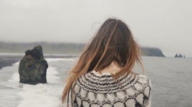 İzlanda, rüzgarda sallayarak saç görünürde deniz kıyısında ayakta ve trol üzerinde seyir genç esmer kadın ayak