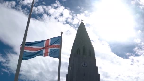 Gyönyörű kilátás nyílik a gyönyörű templom Hallgrimskirkja, Reykjavík, Izland és a nemzeti zászló integet a szél. — Stock videók