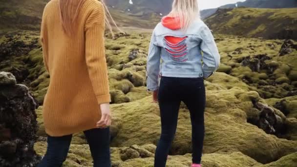 Back view of two tourists woman hiking together in Iceland. Girls walking through the lava field covered moss. — Stock Video