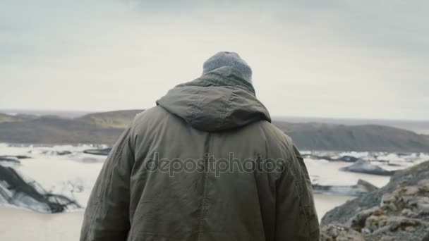 Junger schöner Mann wandert in den Bergen in der Nähe der Vatnajokull-Eislagune und blickt auf die Gletscher in Island. — Stockvideo