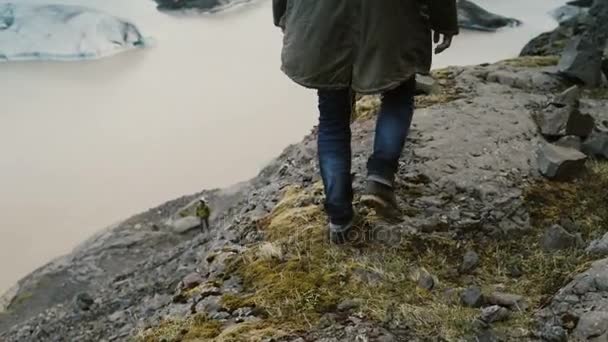 Junger gutaussehender Mann, der durch die Felsen in den Bergen nahe der Eislagune Vatnajokull in Island geht. — Stockvideo