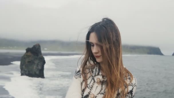 Porträt einer jungen schönen nachdenklichen Frau, die am schwarzen Strand steht, in der Nähe der Troll-Zehen-Felsen in Island. — Stockvideo