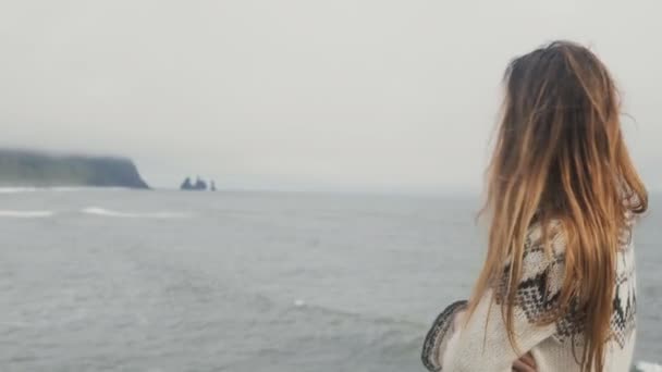 Mladá krásná žena stojící na černou pláž, usmíval se a kochat výhledem na skály prsty troll v Islandu. — Stock video