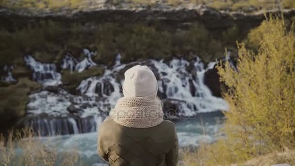 Zadní pohled na mladou ženu stojí v horském údolí a při pohledu na vodopády Islandu, poznávání přírody. — Stock video