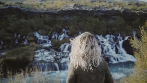 Young traveling woman standing near the waterfalls in Iceland and smiling. Girl raising hands up and feeling happy. — Stock Video