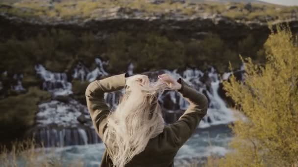 Back view of young traveling woman standing in mountains valley and looking on waterfalls in Iceland alone. — Stock Video
