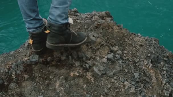 İzlanda'daki güçlü bir şelale yakınındaki kayada duran ve su akışı düşen arıyorum genç kadın. — Stok video