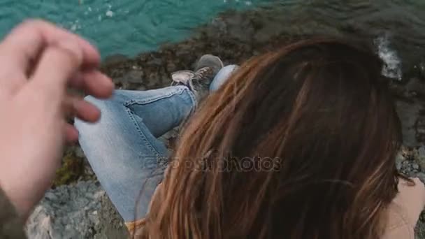 Horní detailní pohled mladá bruneta žena sedící na skále a při pohledu na vodě, člověk dělá, dotýká její vlasy. — Stock video
