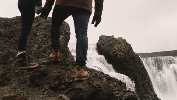 Ung man och kvinna som står på en kulle efter vandring och tittar på en kraftfull vattenfall på Island, berömda syn. — Stockvideo