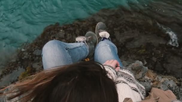 Close-up bovenaanzicht van jonge brunette vrouw zit op rock en op zoek op het blauwe water, haren wuiven in de wind. — Stockvideo