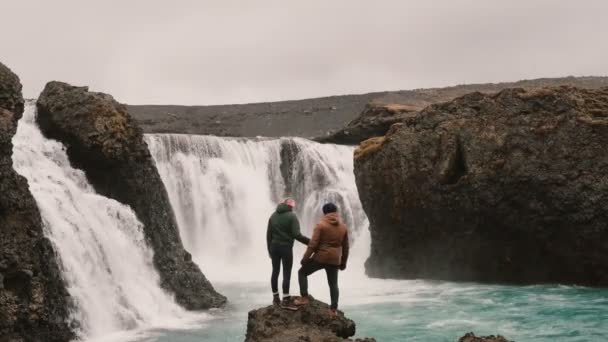 Frihet: lyckliga paret efter vandring står nära vattenfallet i Island och höja händerna tillsammans. — Stockvideo
