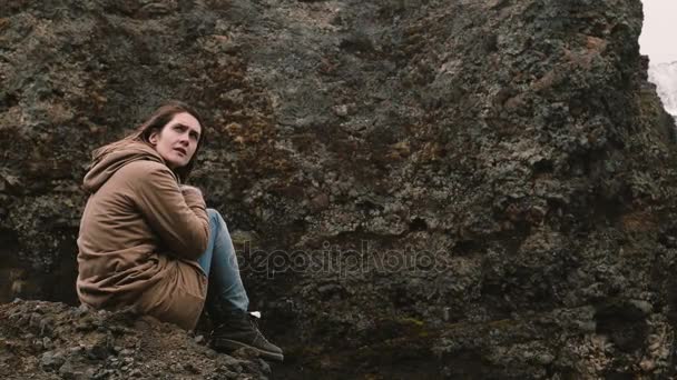 Ung vacker kvinna sitter på klippan i bergen och tänkande ensam. Turist vila efter vandring i Island. — Stockvideo