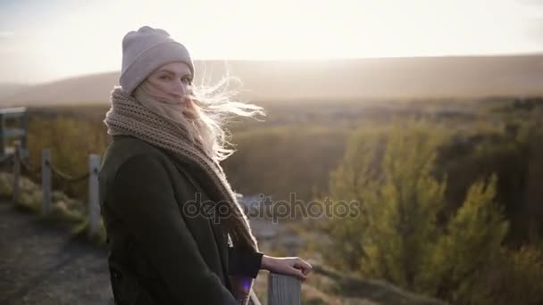 Junge schöne Frau, die an einem kalten, sonnigen Tag auf der Brücke steht und die Landschaft genießt. Haare wehen im Wind. — Stockvideo