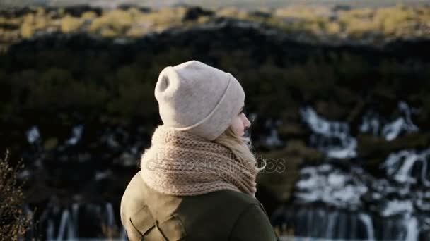 Свобода: вид сзади молодой красивой женщины, стоящей у водопада Барнафосс в Исландии, прыгающей и поднимающей руки . — стоковое видео