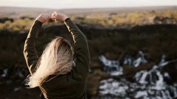 Vista posterior de la joven rubia de pie cerca de la cascada de Barnafoss en Islandia y disfrutando del hermoso paisaje . — Vídeo de stock