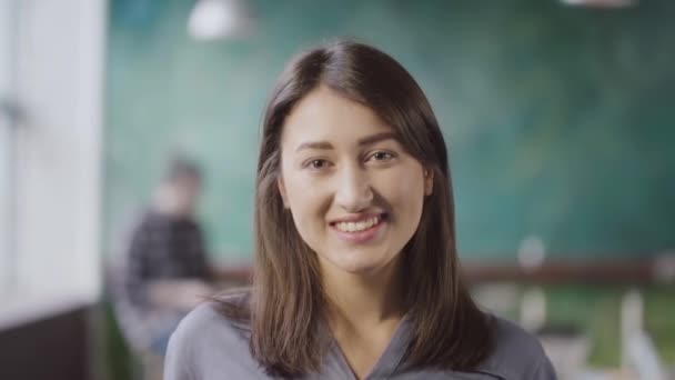 Retrato de una hermosa mujer asiática en una oficina moderna. Joven empresaria exitosa mirando a la cámara, sonriendo . — Vídeos de Stock