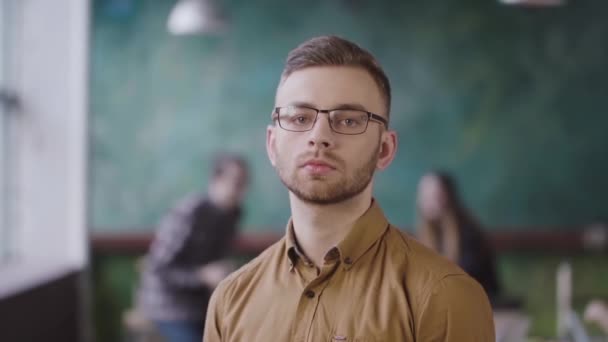 Portrait of young serious businessman at busy office. Handsome male employee looking at camera — Stock Video