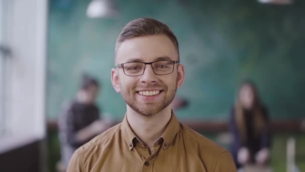 Retrato de un joven empresario exitoso en una oficina ocupada. Hombre guapo empleado mirando a la cámara y sonriendo . — Vídeo de stock