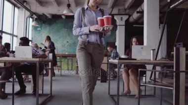 Esmer kadın Yöneticisi modern ofise geliyor. Genç kadın meslektaşları ile selamlıyor, arkadaşıma kahve getiriyor. yavaş mo