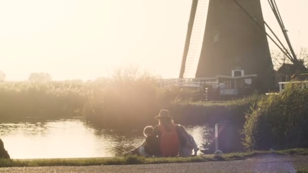 석양에 작은 호수 근처 두 아이와 어머니. 부두에 함께 백인 가족의 평화로운 보기. 4 k 다시 보기. — 비디오