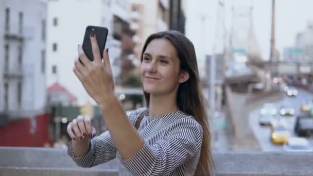 Молода щаслива красива жінка фотографує селфі на смартфоні, дорога з машинами та таксі на фоні . — стокове відео