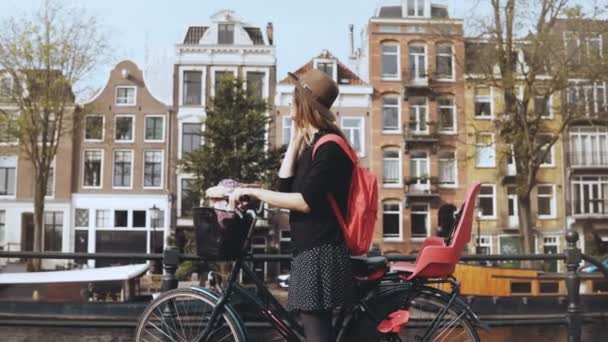 Улыбающаяся леди разговаривает по телефону, уезжает на велосипеде. Молодая деловая женщина на великолепном мосту. Амстердам, Нидерланды. 4K — стоковое видео