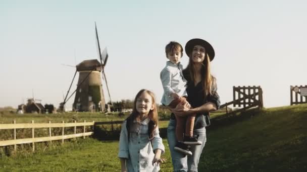 Mulher caucasiana com dois filhos perto de um parque eólico. Mãe, menino e menina bonito explorar o ambiente juntos. 4K . — Vídeo de Stock