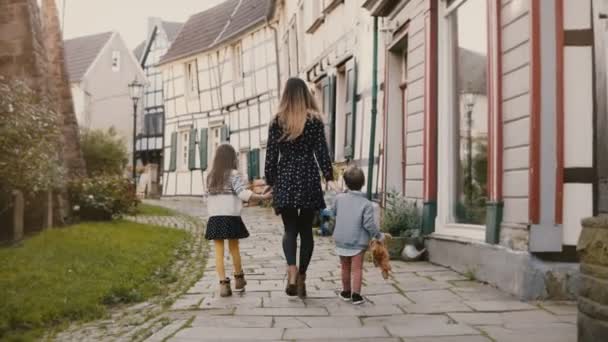 Женщина идет с мальчиком и девочкой, держась за руки. Мама, двое маленьких детей. Половинчатые дома Хаттинген Германия. 4K . — стоковое видео