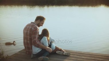 İki çocuklu beyaz adam su kuşları izlemek. Mutlu baba ve çocukların birlikte bir gün batımı göl iskelede oturup. Çocukluk. 4k.
