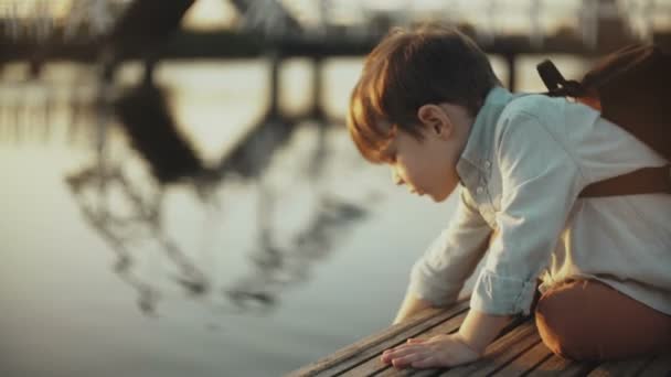 Aranyos európai fiú játszik a tó víz a mólón. Kis férfi gyermek hátizsák nyári természet felfedezéséhez. 4 k közelről. — Stock videók