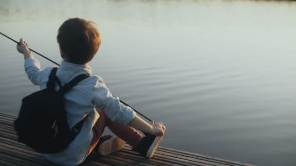 Lindo chico europeo juega con un palo en el muelle del lago. Niño pequeño con mochila disfrutando de las vacaciones. Feliz infancia. 4K . — Vídeos de Stock