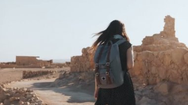 Kadın sırt çantası ile antik duvarlar arasında yürüyor. Çekici beyaz kadın turist dağ panorama sahiptir. Masada. 4k.