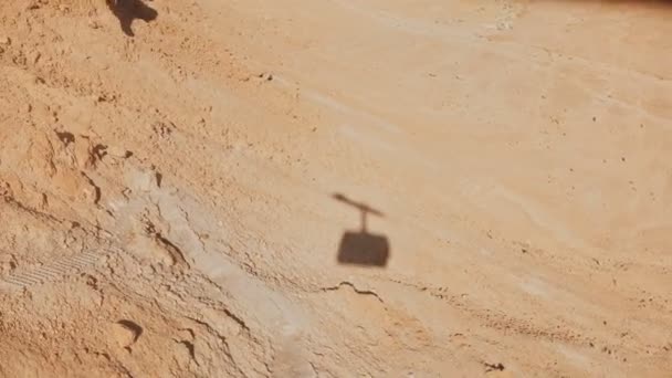 Ombre d'une cabane à câbles s'élevant dans le désert de Masada. Téléphérique aérien qui monte par une journée ensoleillée. Du sable et des pierres. Israël 4K . — Video