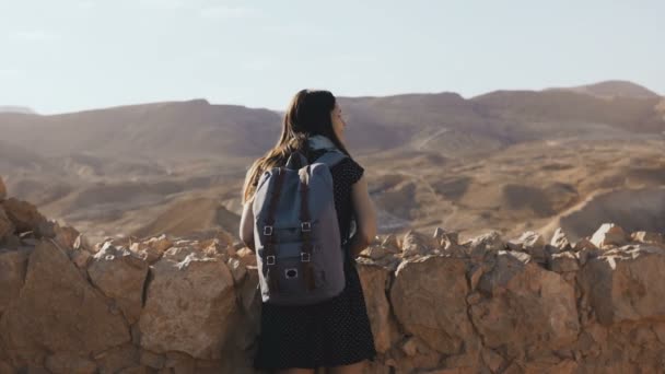 Girl with backpack looks at mountain panorama. Attractive European woman explores ancient ruins. Masada, Israel. 4K. — Stock Video