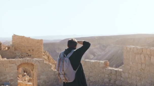 European man takes photos of ancient scenery. Male tourist with camera and backpack explores mountain ruins. Israel 4K. — Stock Video