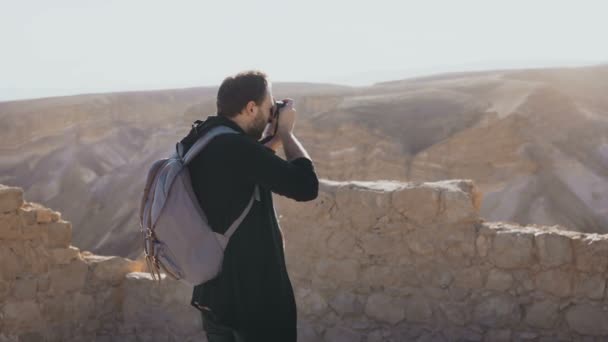 Male photographer walks along ancient Israel ruins. Road to Masada fortress. Young man with backpack takes photos. 4K. — Stock Video