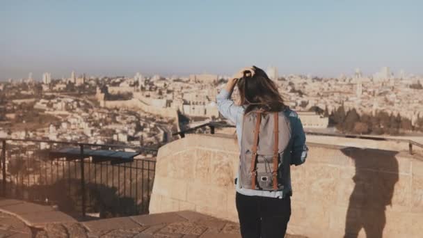 Woman with backpack comes up to Jerusalem panorama. Excited Caucasian tourist looks at ancient old town in Israel. 4K. — Stock Video