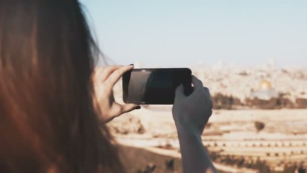 Chica toma fotos de teléfonos inteligentes de Jerusalén, Israel. Manos femeninas sosteniendo el teléfono en un día soleado. Capturando momentos. 4K . — Vídeos de Stock