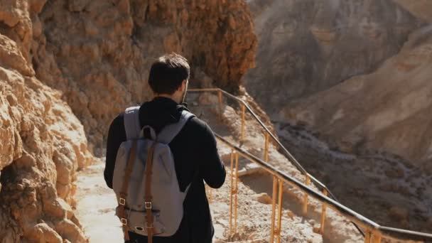 Turista masculino caucásico en la antigua carretera de montaña. El hombre con smartphone y cámara disfruta de ruinas históricas del desierto de Israel. 4K — Vídeo de stock