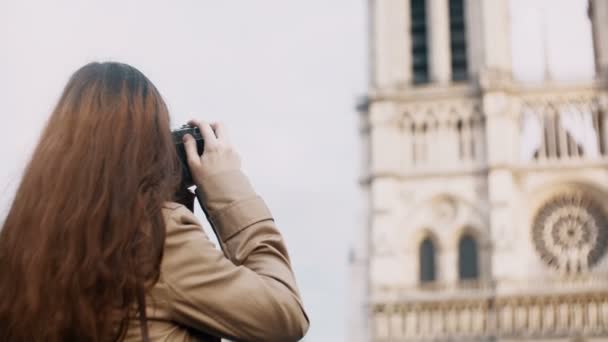 Brunette teenager taking photo of Notre Dame on retro film camera, exploring the famous places of Paris, France. — Stock Video