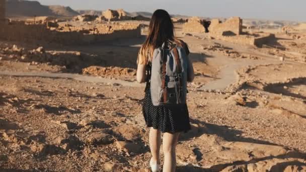 Γυναίκα με σακίδιο εξερευνά αρχαία ερείπια της ερήμου. Όμορφα ευρωπαϊκά τουριστικά βόλτες σε βράχους και άμμο. Ισραήλ Masada 4k. — Αρχείο Βίντεο