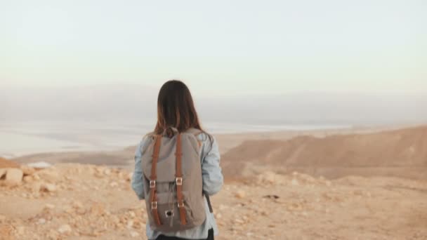 Vrouw met rugzak wandelingen in bewolkt woestijn. Meisje met doordachte Kaukasische dwaalt op droog zand, glimlachend. Israël 4k. — Stockvideo