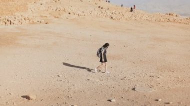 Harabeleri ıssız kadın sırt çantası ile yürür. Kuru kum, kaya, duvarlar üzerinde genç Kafkas kadın gezgin. Masada İsrail 4k.