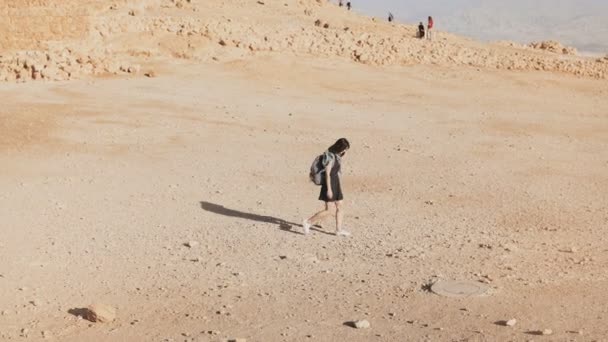 Mulher com mochila caminha para ruínas do deserto. Jovem viajante caucasiana em areia seca, pedras, paredes. Masada Israel 4K . — Vídeo de Stock