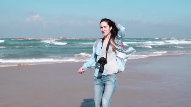 Mulher europeia bonita caminha na praia ensolarada. Menina bonita olha para a câmera sorrindo. Vento a soprar no cabelo. Movimento lento — Vídeo de Stock