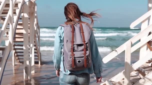 Girl walks by white stairs to sunny sea shore. Freedom. Hair blowing in wind. Woman with backpack on beach. Slow motion. — Stock Video