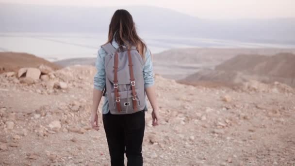 Woman with backpack walks in desert. Slow motion. Young girl wanders on dry sand and rocks. Amazing mountain scenery. — Stock Video