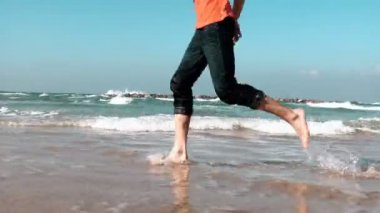 Yakın çekim erkek bacaklar deniz kıyısı yaz plaj boyunca çalıştırın. Özgürlük kavramı. Düşük açılı yan görünüm. Tatil keyfini adam. 4k