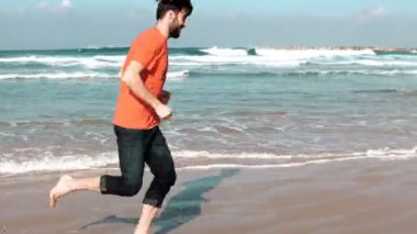 Deniz kumsalda koşan Avrupa sakallı adam. Özgürlük kavramı. Erkek turist şaşırtıcı yaz sahil üzerinde yalınayak çalışır. 4k.